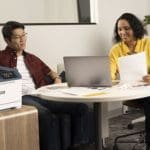 Xerox® C410 Imprimante couleur en situation au travail Deux personnes au bureau à côté de l'imprimante couleur Xerox® C410